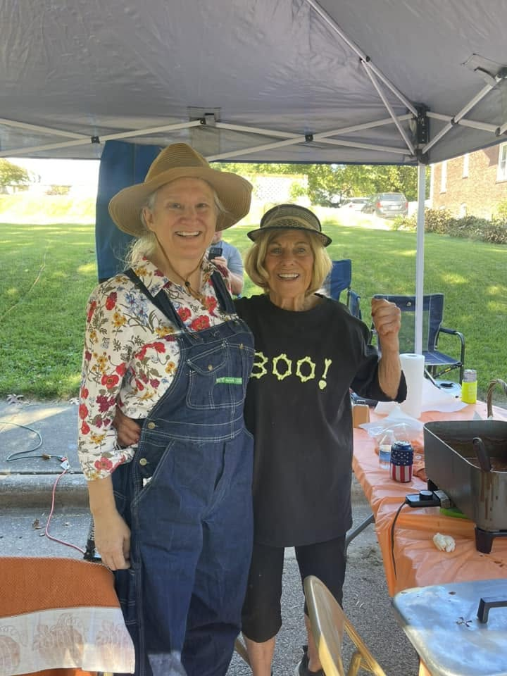 Two Harvest Hoedown volunteers smiling beneath a canopy