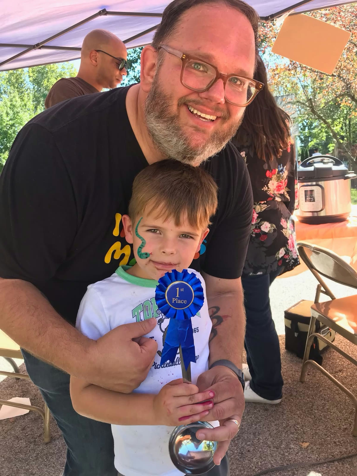 A child holding a blue first-place ribbon with an adult